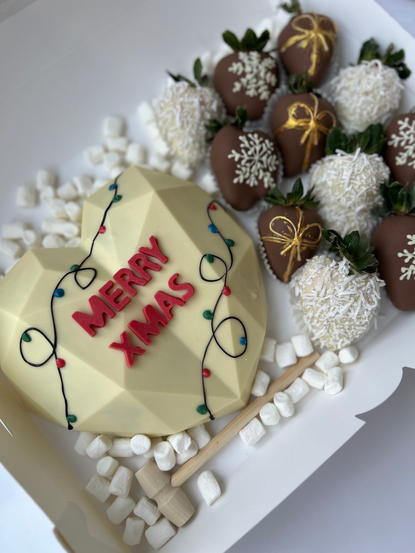 Geometric cake with 'Merry Xmas' decoration, surrounded by chocolate-covered strawberries and marshmallows on a white plate.