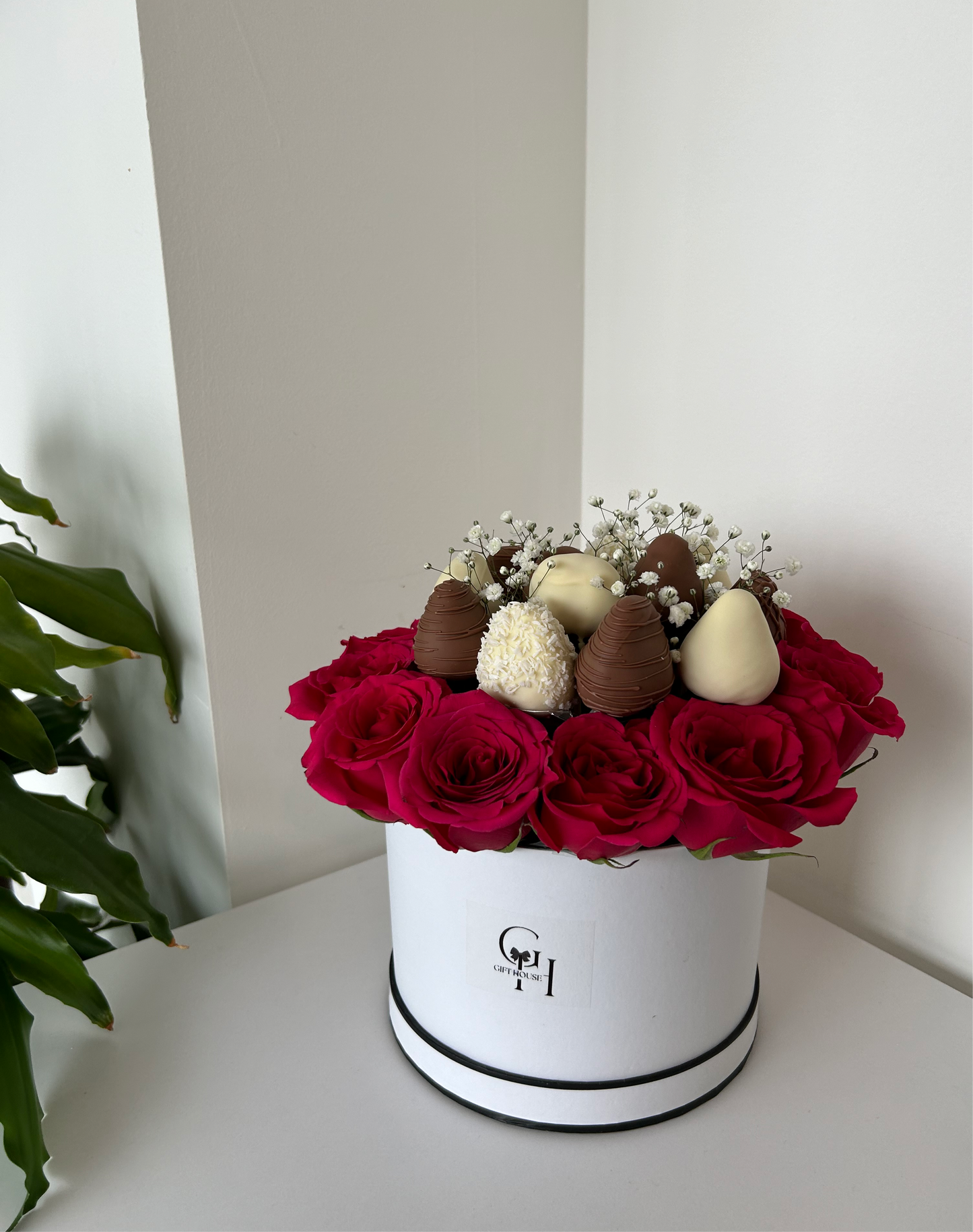 chocolate covered strawberries and red roses in white floral box with green leafs on background