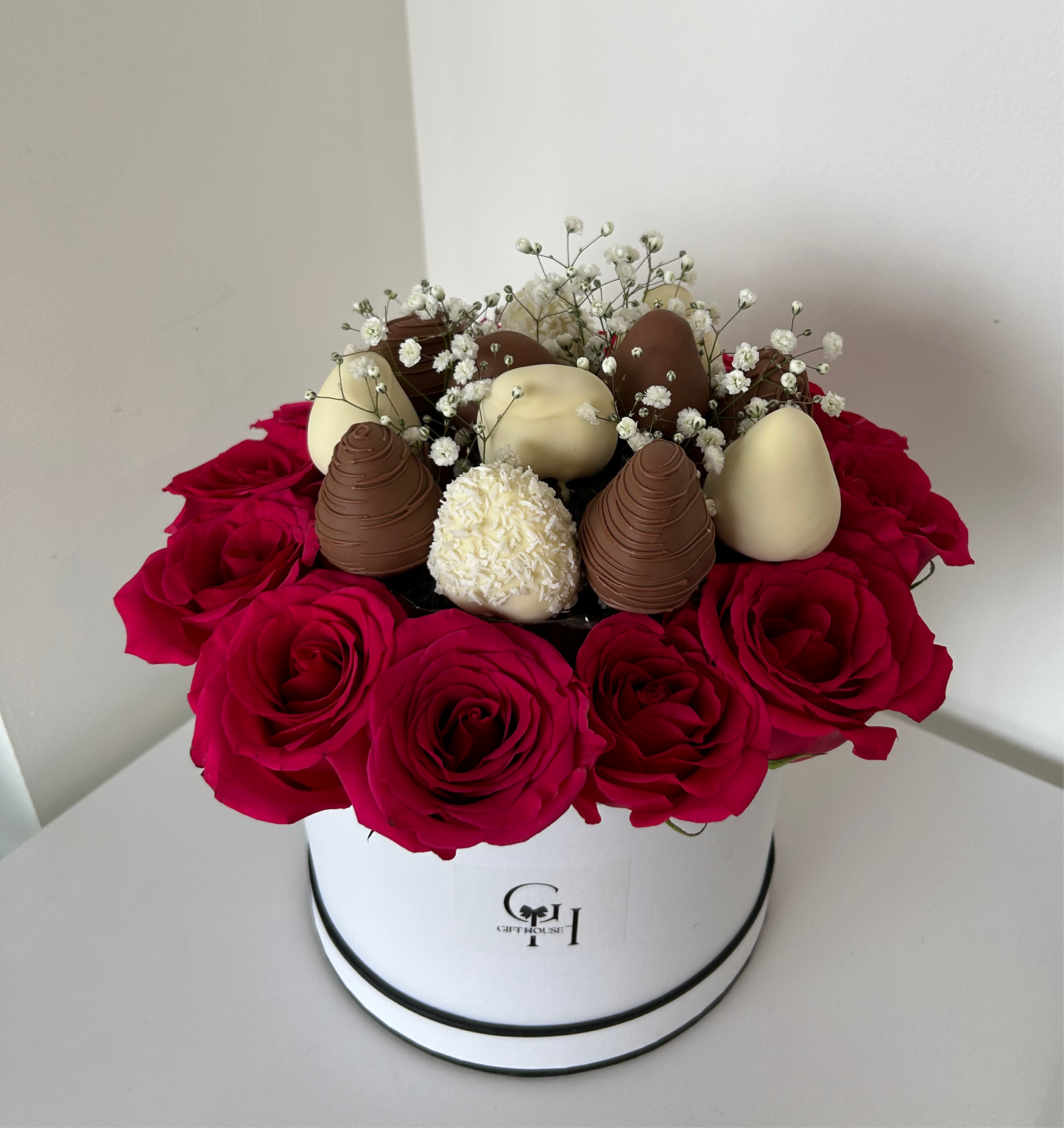 close up of chocolate covered strawberries and red roses in white floral box 
