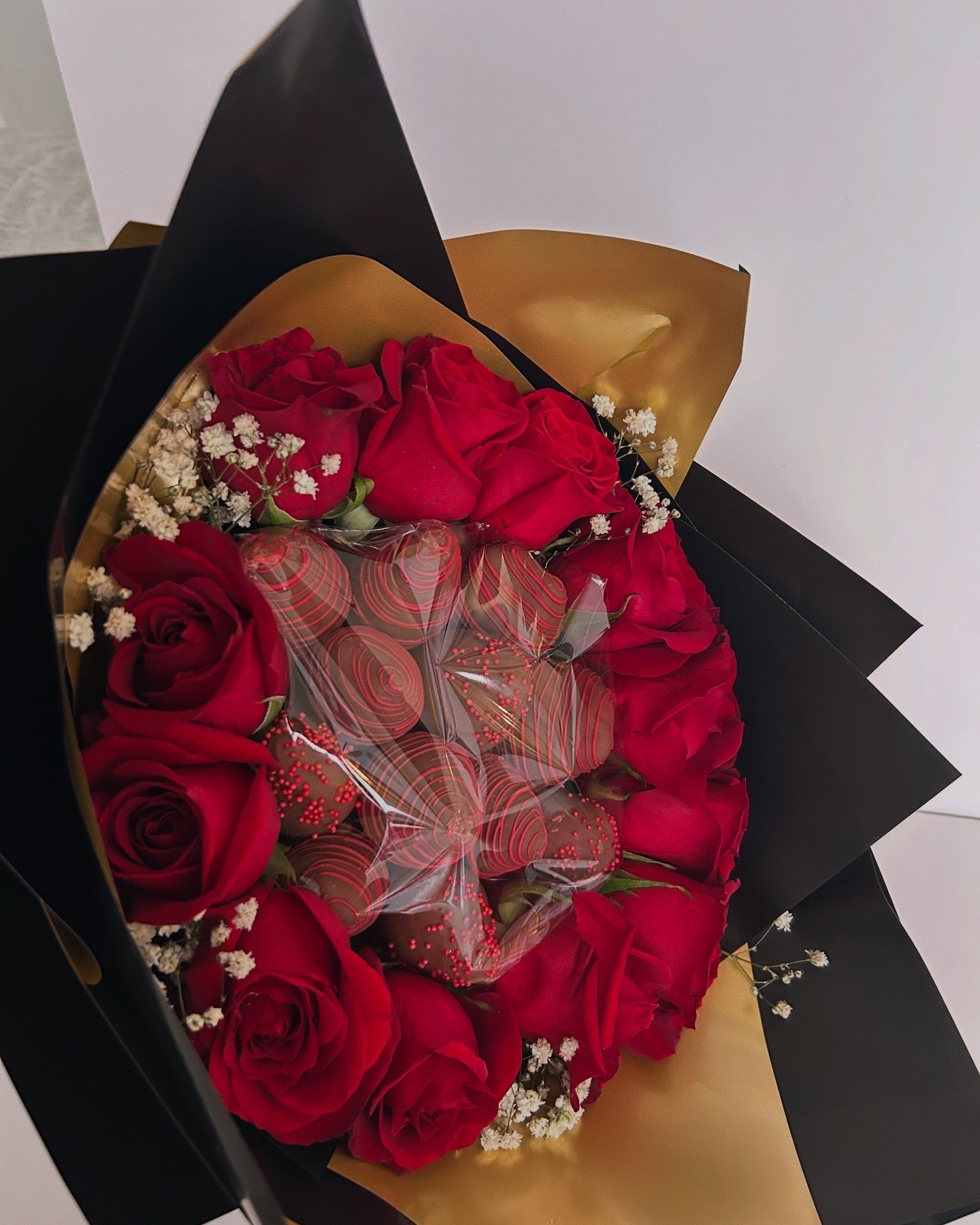 close-up of Bouquet of chocolate covered strawberries and roses with black and gold wrapping 