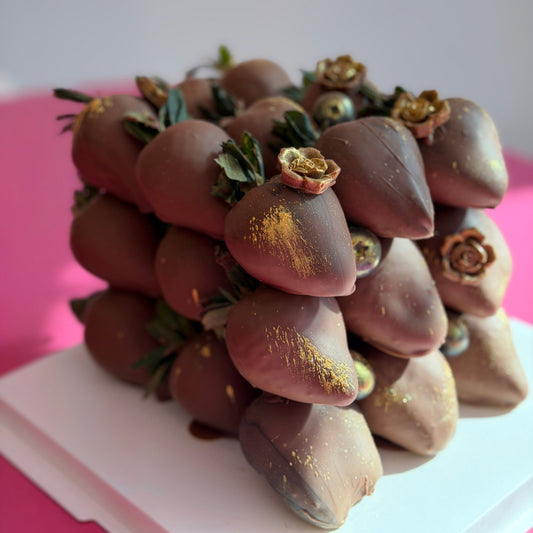 Chocolate-covered strawberries with gold dust on a white surface with a pink background