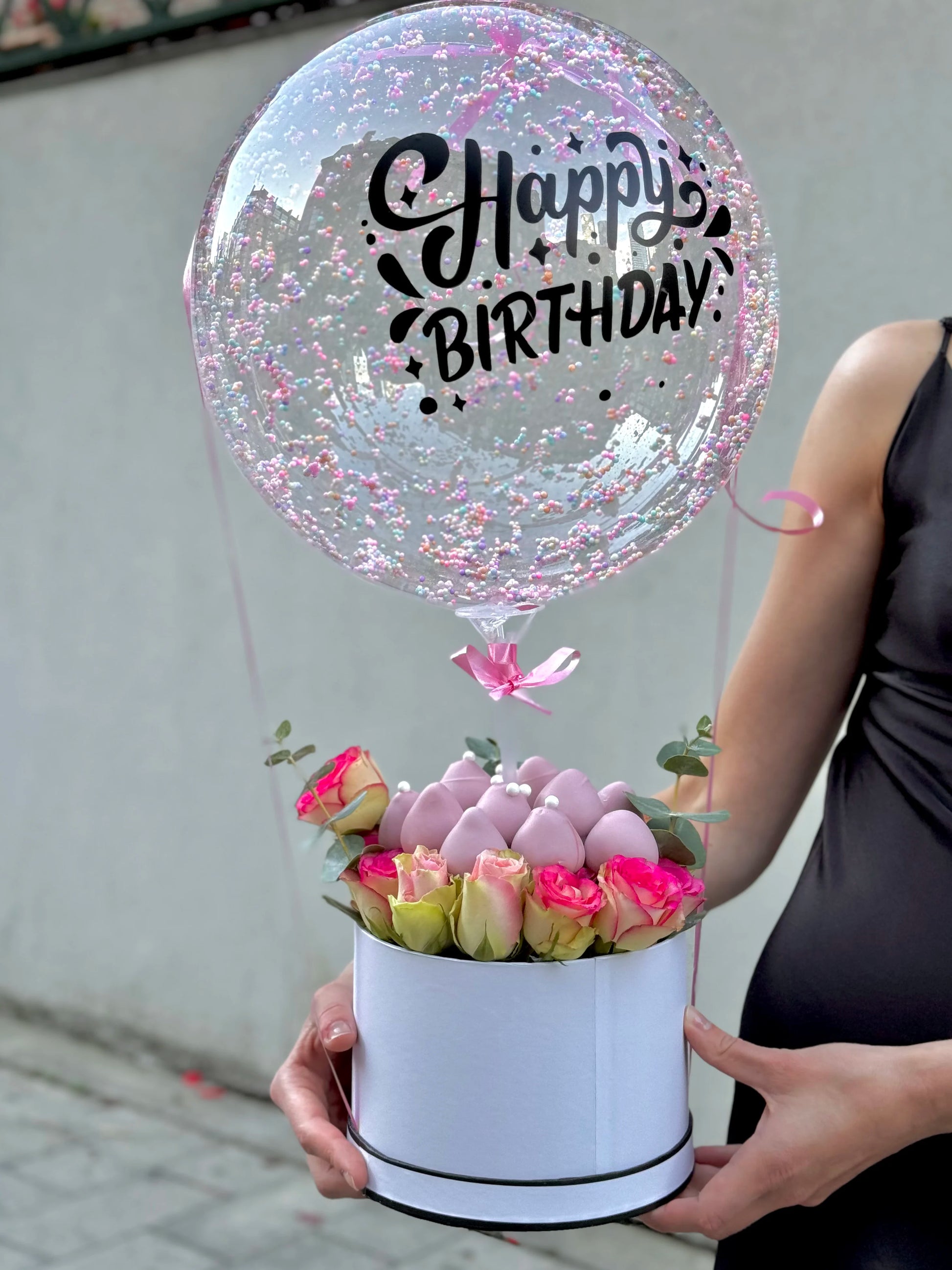 model holds box wth roses and chocolate covered strawberries with bobo balloon on top 