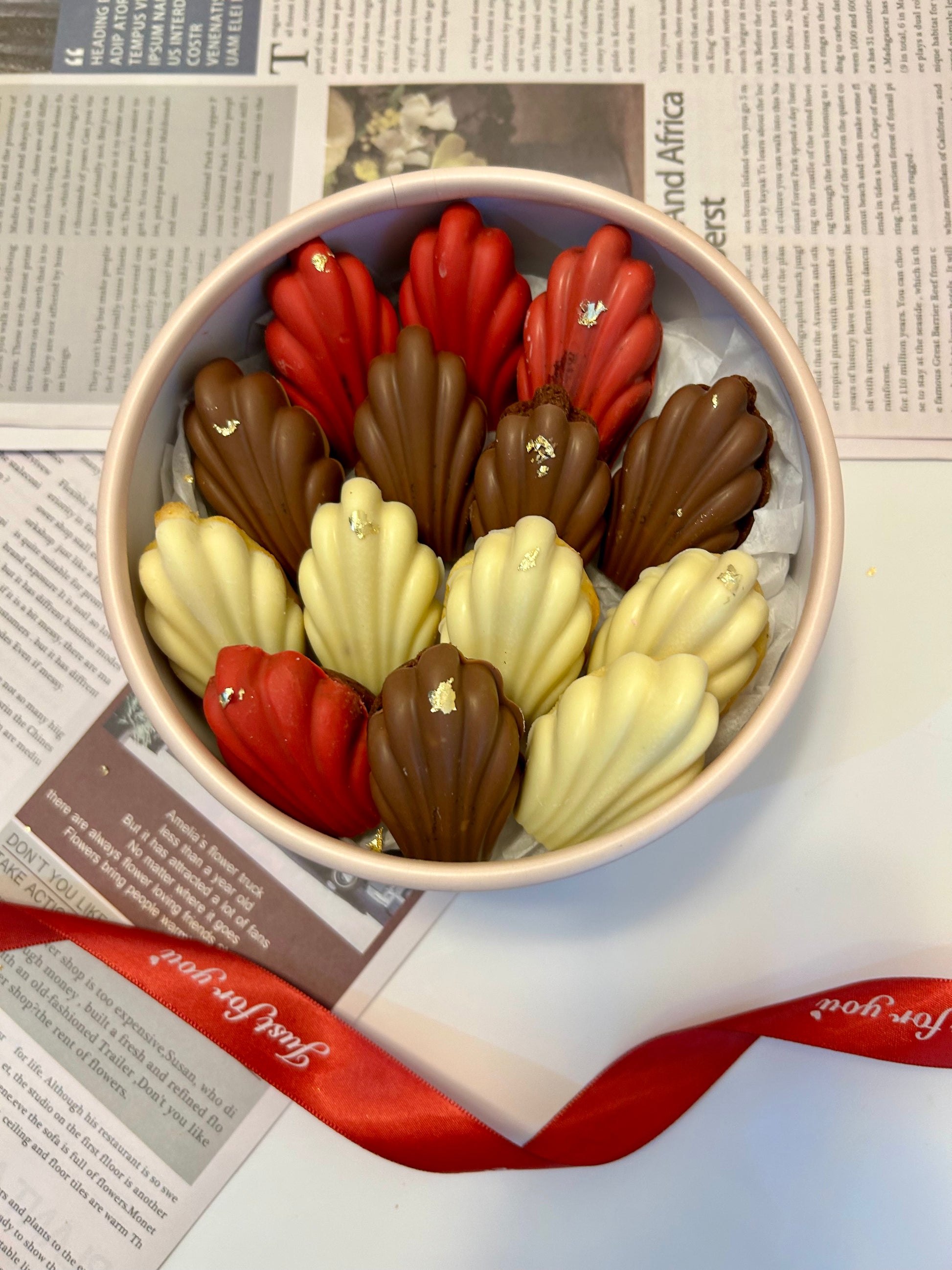 Madeleines in round box with red ribbon on background 
